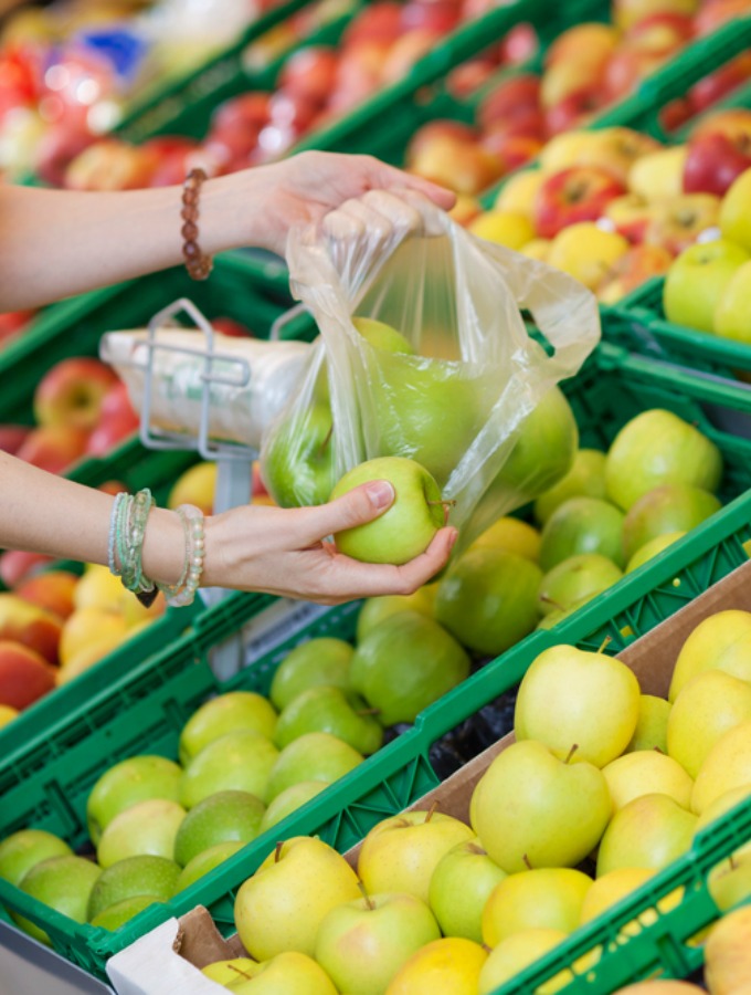 Closeup image of a female customer picking green apples to buy.